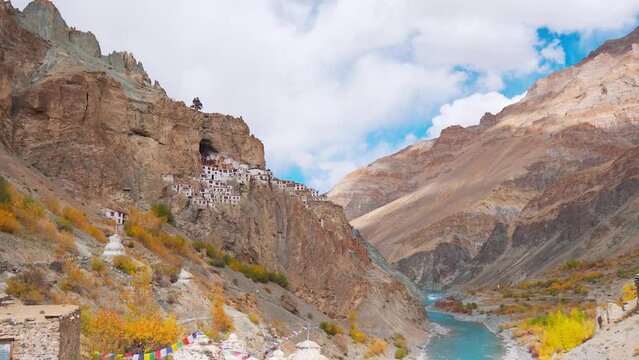 Zoom out shot of Phugtal monastery in remote Himalayan mountains with flowing Tsarap chu river and autumn trees. Ancient monastery made in a cave more than 2550 years ago in India.
