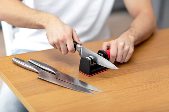 Close-up photo of man sharpening knives with special knife sharpener at home