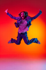 Fototapeta na wymiar Funny portrait of emotive, young girl wearing casual clothes levitating in air over red color studio background in neon light. Freedom