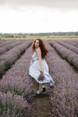 Beautiful girl in dress running and flying long hair on violet lavender field. Woman walk on sunset. Enjoy floral glade, summer nature. .Female on background of lavender. France, Provence. Back view.