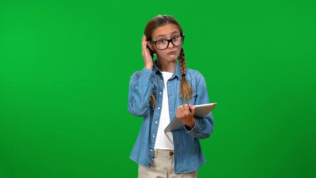 Intelligent smart adolescent girl scrolling digital tablet looking at camera with surprised facial expression and gesturing thumb up smiling. Confident Caucasian teenager posing on green screen