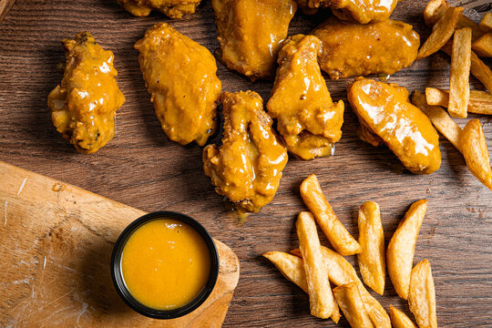 alitas con salsa miel mostaza regadas en una meza con papas a la francesa