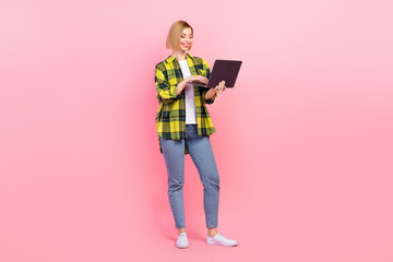 Full size photo of pretty young girl hold netbook ecommerce ordering wear trendy plaid yellow clothes isolated on pink color background