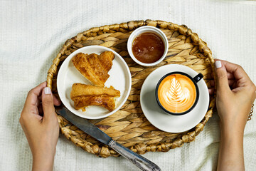 closeup hands woman holding a tray contains Morning breakfast in bed with coffee and apricot cookies, red rose flower and cup of latte art coffee