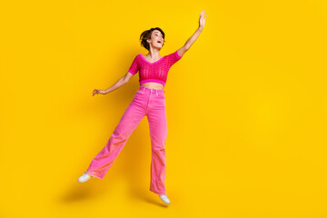 Full length photo of impressed nice carefree woman wear pink knit top pants jumping look empty space isolated on yellow color background