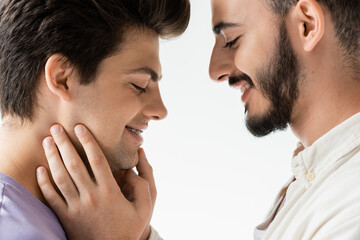 Side view of positive bearded gay man in casual shirt touching face of young partner with braces on...