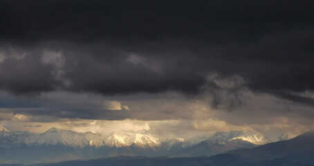 Montagne innevate illuminate dal sole squarciano le nuvole nere prima della tempesta