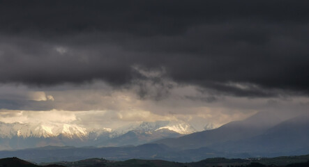 Montagne innevate illuminate dal sole squarciano le nuvole nere prima della tempesta