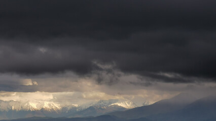 Montagne innevate illuminate dal sole squarciano le nuvole nere prima della tempesta