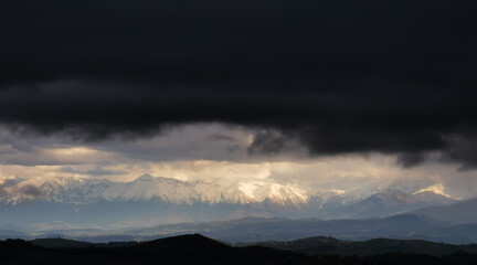 Montagne innevate illuminate dal sole squarciano le nuvole nere prima della tempesta
