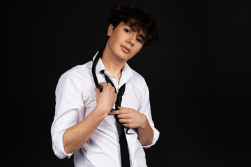 Young handsome man in white shirt with a black snake crawling on his shoulder. Isolated on black background.