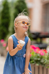a little happy girl with down syndrome eats ice cream in the summer on a walk