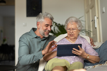 Mature man learning his senior mother working with digital tablet.