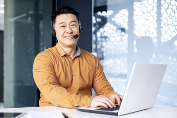 Portrait of successful office worker with headset for video call, asian man smiling and looking at...