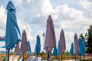 Folded beach umbrellas. Preparing the beach for the new opening season. Lots of beach umbrellas next to the water pool. The concept of tourist vacation and vacation. © Anat art