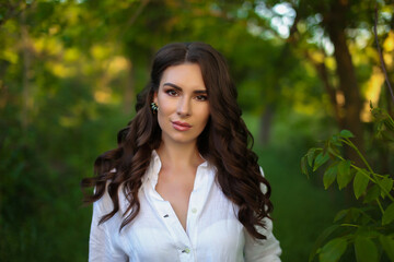 beautiful fashionable brunette woman adult  posing in the park on the nature backgraund in white linen shirt