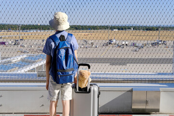 child in outdoor terrace of airport, young traveler is waiting for boarding, boy of 8-10 years old in blue shirt with suitcase and teddy bear, concept of vacation, long journey, air travel insurance