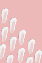 Lots of smears of cosmetic cream. Light, smooth surface. Texture of spreadable cream. Liquid creamy strokes. On a pink background. Cosmetic background, banner.