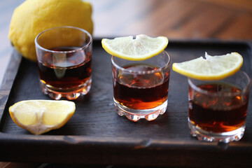 three shot glasses with lemon slices on a wooden plate