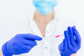 A doctor preparing a vaccine syringe in blue gloves and a mask for a covid 19 vaccination