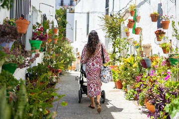 mother walking with a baby carriage along a street full of flowers during summer