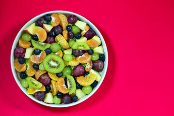Healthy fresh fruit salad bowl on red background. Top view. Healthy food concept, healthy high vitamin fruit, mixed fruit background.