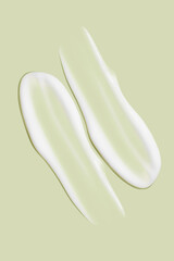 Lots of smears of cosmetic cream. Light, smooth surface.  In a row. At an angle. Top view. Texture of flowing cream. Liquid creamy strokes. On green background. Cosmetic background, banner.