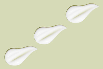 Lots of smears of cosmetic cream. Light, smooth surface.  In a row. At an angle. Top view. Texture of flowing cream. Liquid creamy strokes. On green background. Cosmetic background, banner.