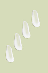 Lots of smears of cosmetic cream. Light, smooth surface.  In a row. At an angle. Top view. Texture of flowing cream. Liquid creamy strokes. On green background. Cosmetic background, banner.