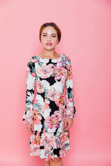a beautiful woman in a floral dress poses on a pink background