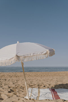 Minimal summer holidays vacation concept. Beach umbrella, beach towel on sand in front of blue sky and sea. Chilling, lounging on the beach