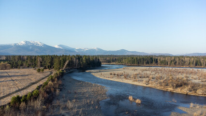 Aerial view of mountain river in taiga. Forest in early spring in sunset time. Siberian or Canadian landscape from above.