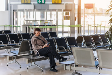 Adult traveler woman sits at airport terminal awaits boarding a flight for departure while uses...