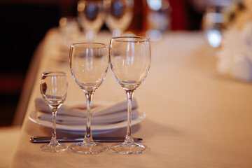 Three crystal or glass goblets on tables served with white ceramic plates and napkins for a banquet at a wedding or other festive event.