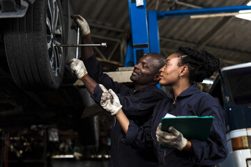 Black mechanic man using tool fixing car tire with black mechanic woman helping in auto repair shop, Car Maintenance