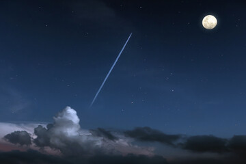 Fototapeta na wymiar Jet plane with contrail flying through clouds in the night sky with full moon glowing and starry