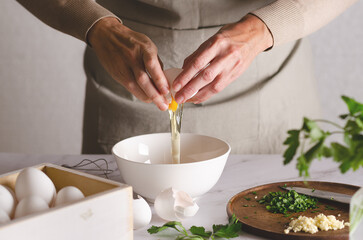 Close up of woman's hands breaking an egg into a bowl with parsley and garlic on a wooden board. The process of preparing Argentinian milanesas.