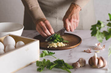 Young woman in a beige apron cuts parsley with a knife. The process of preparing Argentinian...