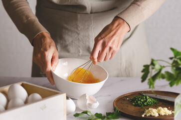 Close up of female hands whisking eggs in a bowl. Parsley and garlic on a wooden board. The process of preparing Argentinian milanesas.