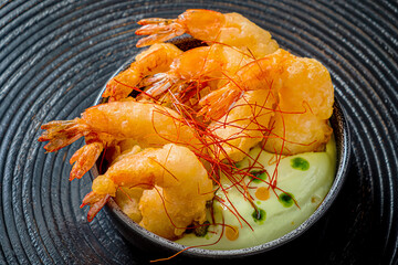 Shrimp tempura on a plate placed against a black background.