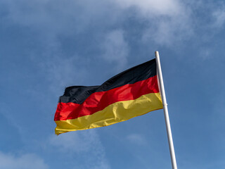 One German flag on a flagpole against a clear blue sky.