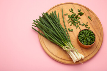 Fresh green onions on a cutting board on pink background.
