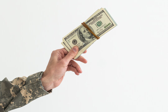A military man in camouflage clothing holds money, dollars in his hand.