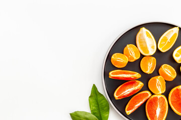 Plate full of fresh citrus fruits with green leaves, top view