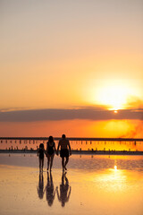 Happy family day. Silhouette of young mom, dad and little daughter holding hands walking together on beach on sunset in summer travel holiday. International Children's Day. Concept of family values.