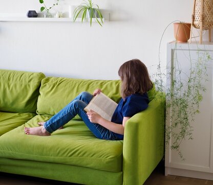 a little girl child is lying on the couch and reading a book at home