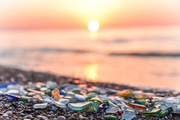Sea glass, Natural polish textured sea glass and stones on seashore. Sunset mediterranean sea coast with waves. Green, blue shiny glass with multi-colored sea pebbles close-up. Beach summer background