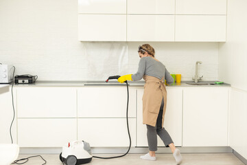 Cropped photo of a woman in uniform cleaning filters for kitchen range hood with steam cleaner while her male colleague working on the background. Cleaning services concept. Housework.