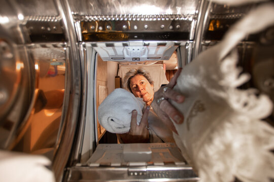 Mujer mediana edad metiendo ropa en la m&aacute;quina de lavar, perspectiva desde adentro de la lavadora