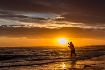 Silhouette of a man fishing on the seashore at the beach during sunset.